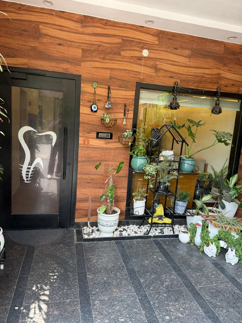 Glass entrance door with tooth logo and plant-lined patio at Poly Dental Clinic Mohali